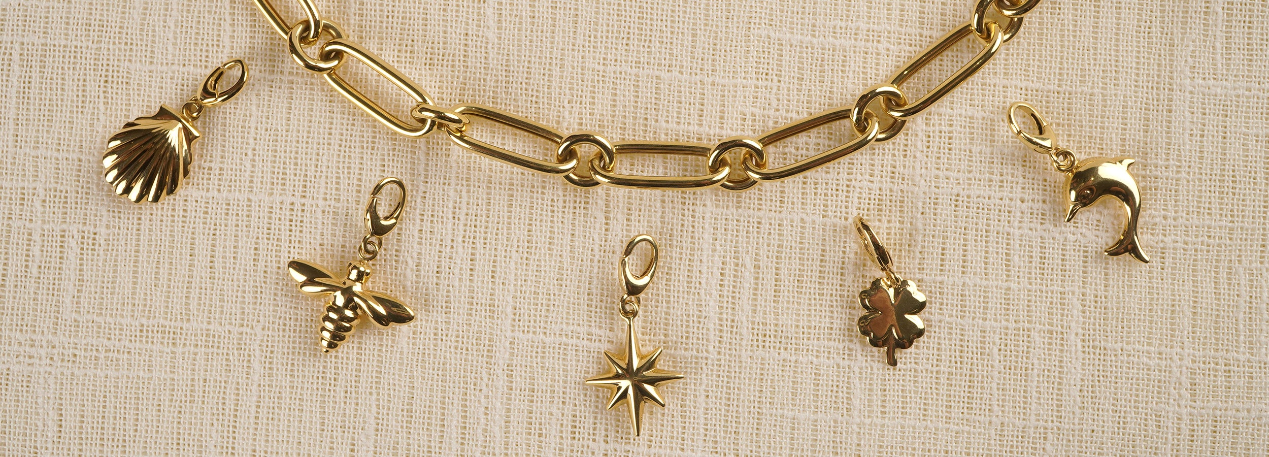 Gold chain bracelet with various charms on a textured beige background